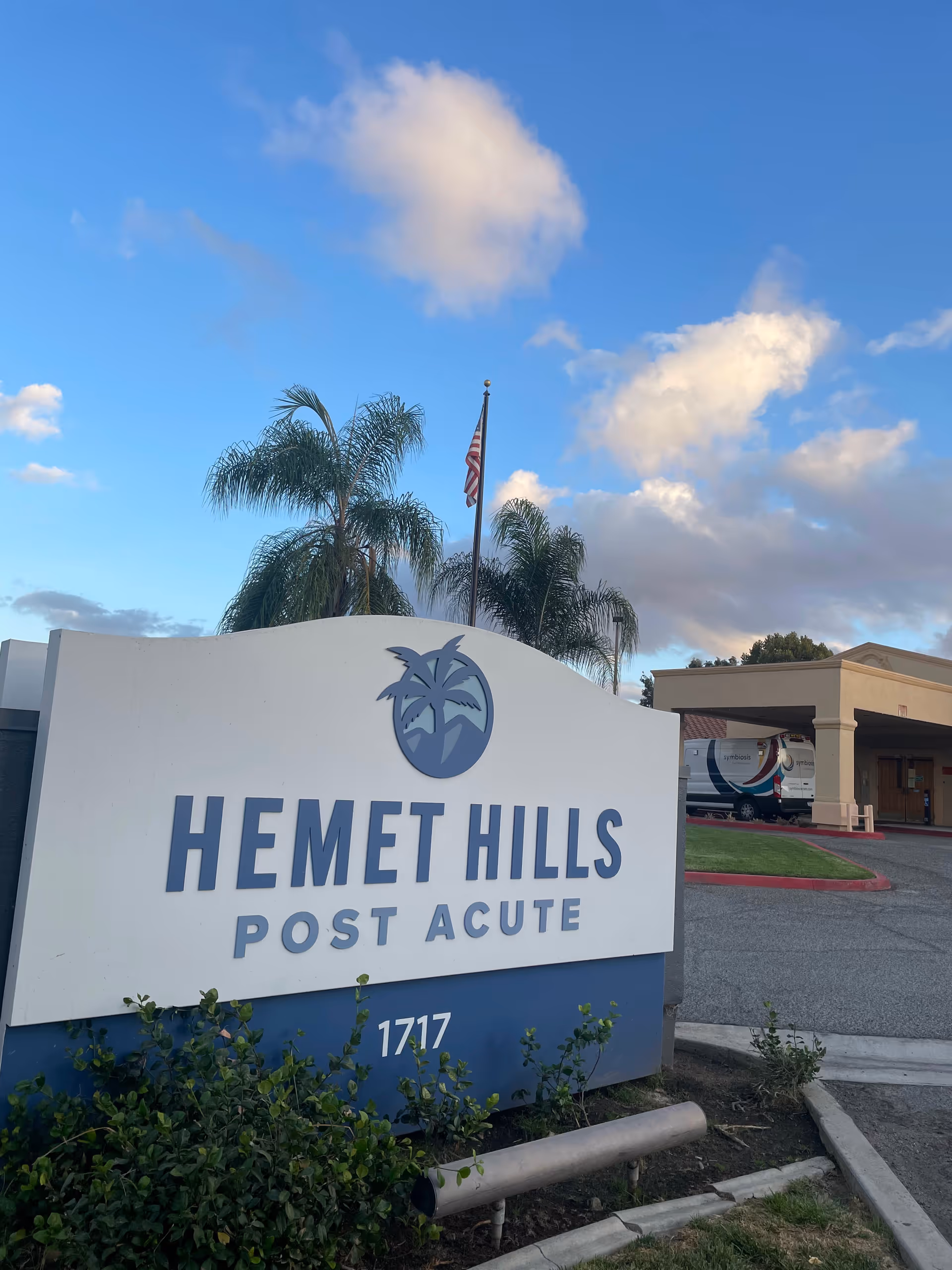 Exterior view of Hemet Hills Post Acute sign with palm trees and American flag.