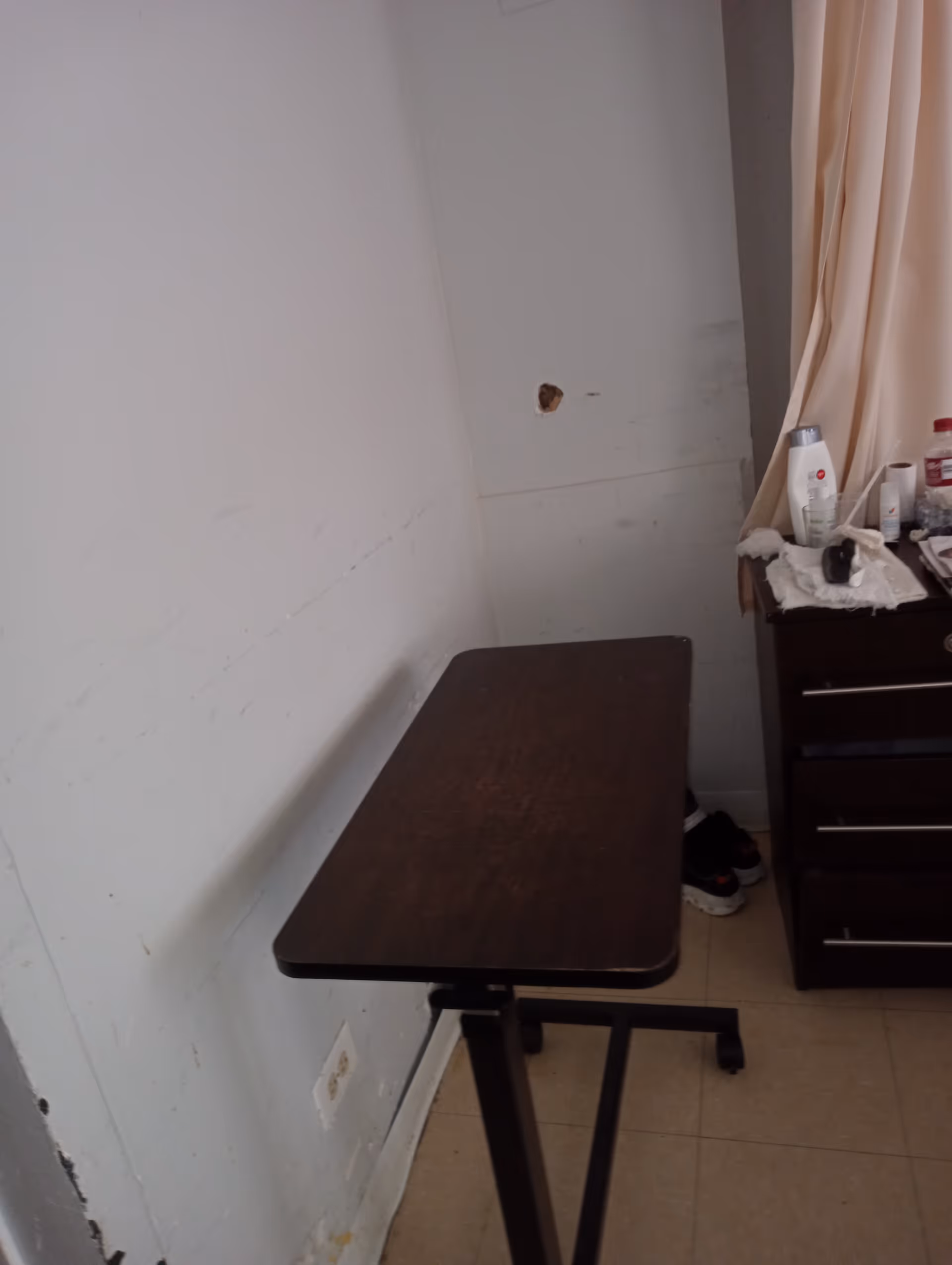 Small, dimly lit corner of a resident room with a wooden table and dresser.