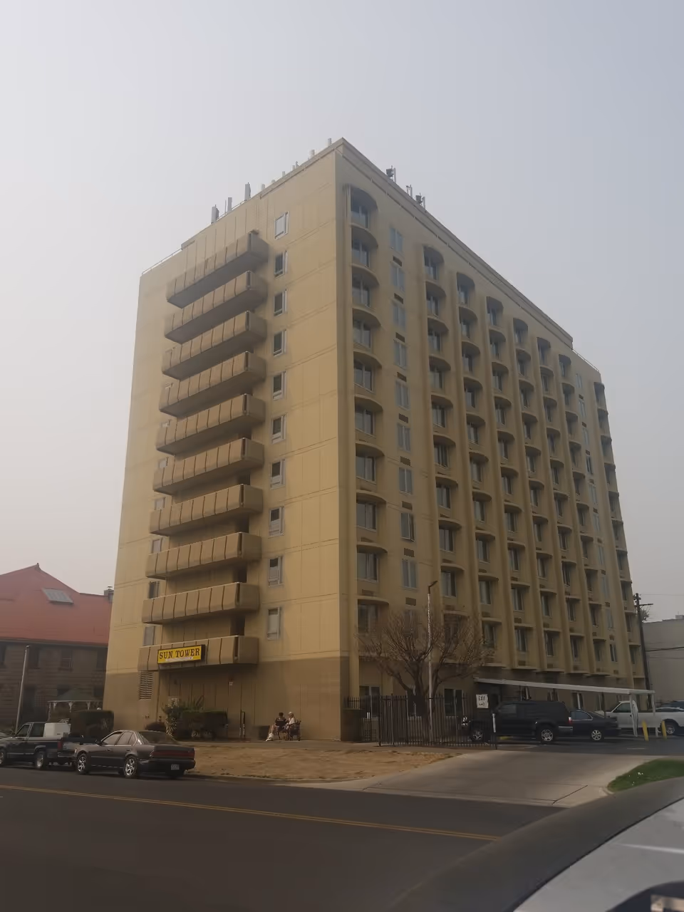 Tall beige multi-story apartment building with balconies and a 'Sun Tower' sign at the entrance, seen from the street.