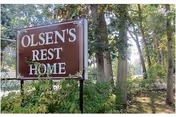 Old sign reading Olsen's Rest Home beside trees near a gated entrance