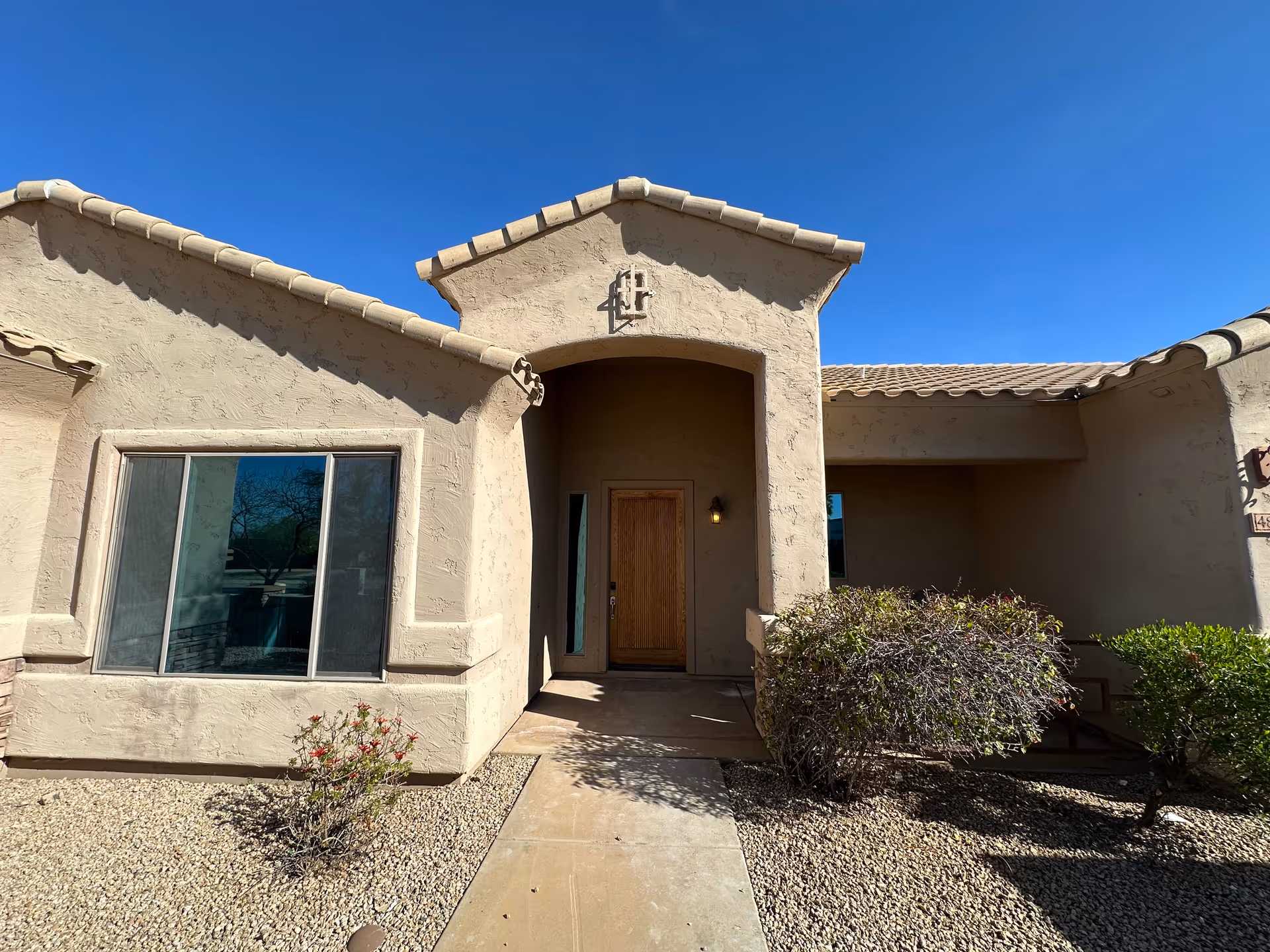 Beige stucco building front entry with wooden door and sparse desert landscaping.