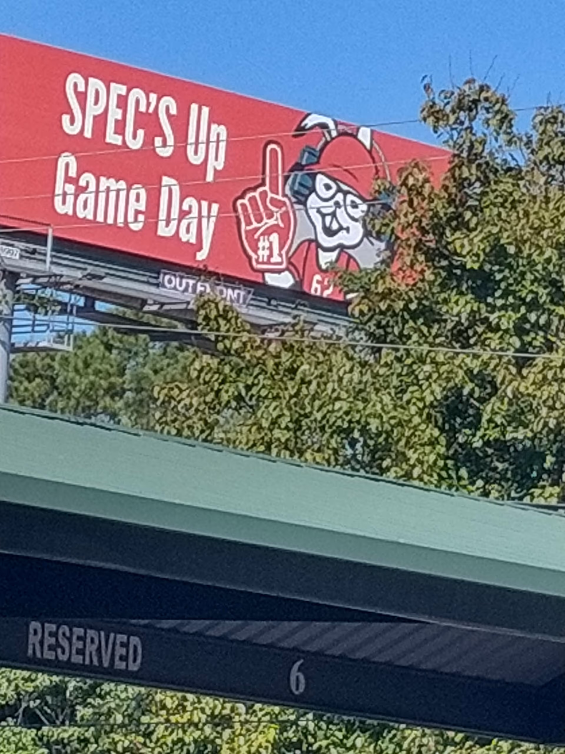 Red billboard on a building exterior with a mascot graphic and trees nearby.