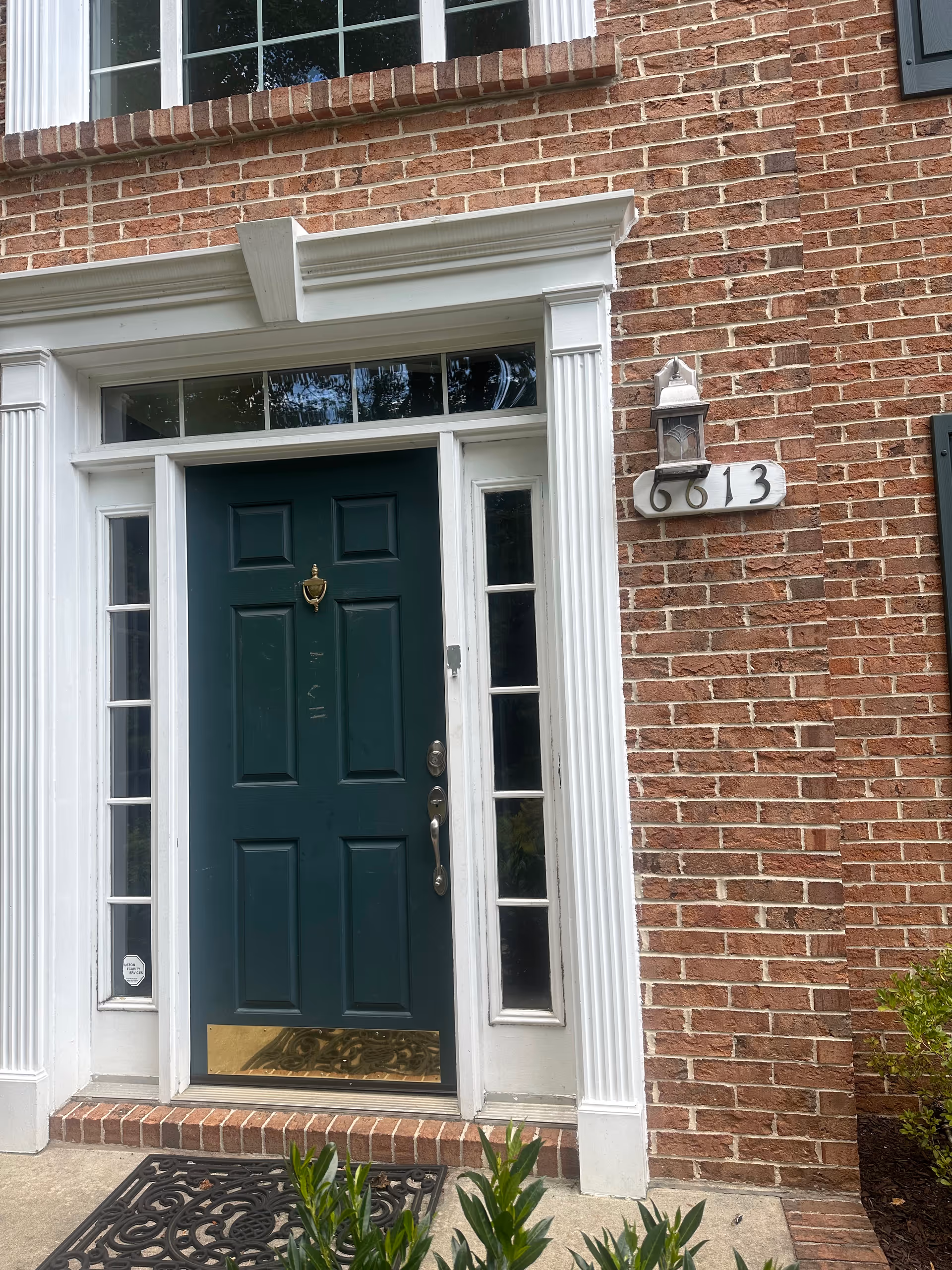Brick building entrance with green door, white trim, and address plaque 6613.