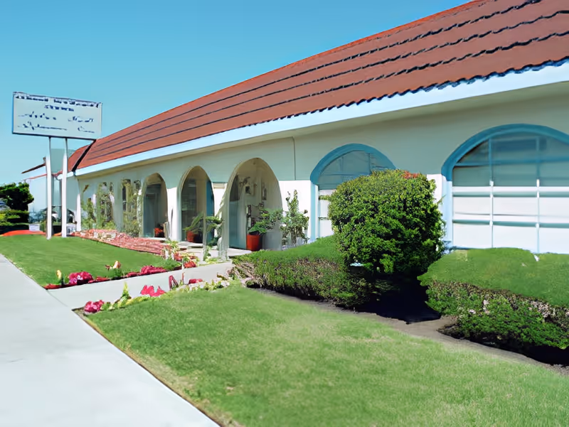 Single-story building with arched entrances, a red tiled roof and manicured lawn and shrubs in front.