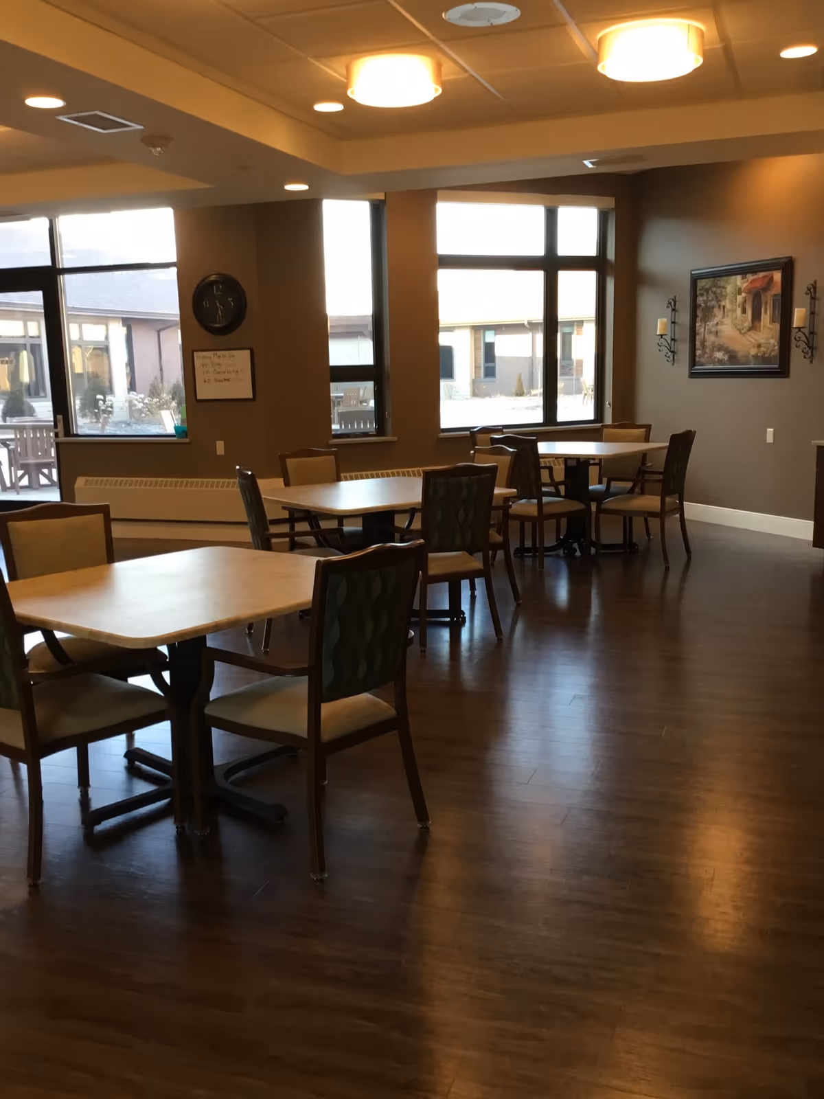 Bright dining area with wooden tables and chairs, large windows, and wall art.