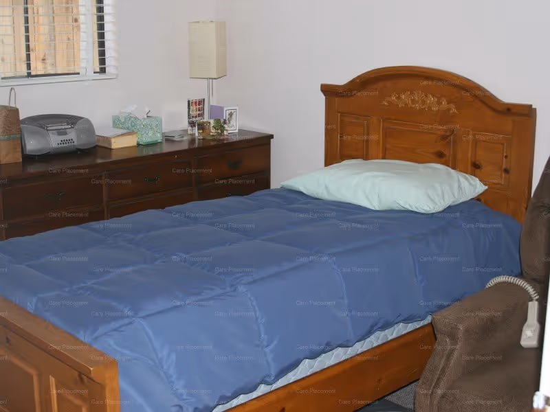 A wooden bedroom with a blue comforter, dresser, and lamp.
