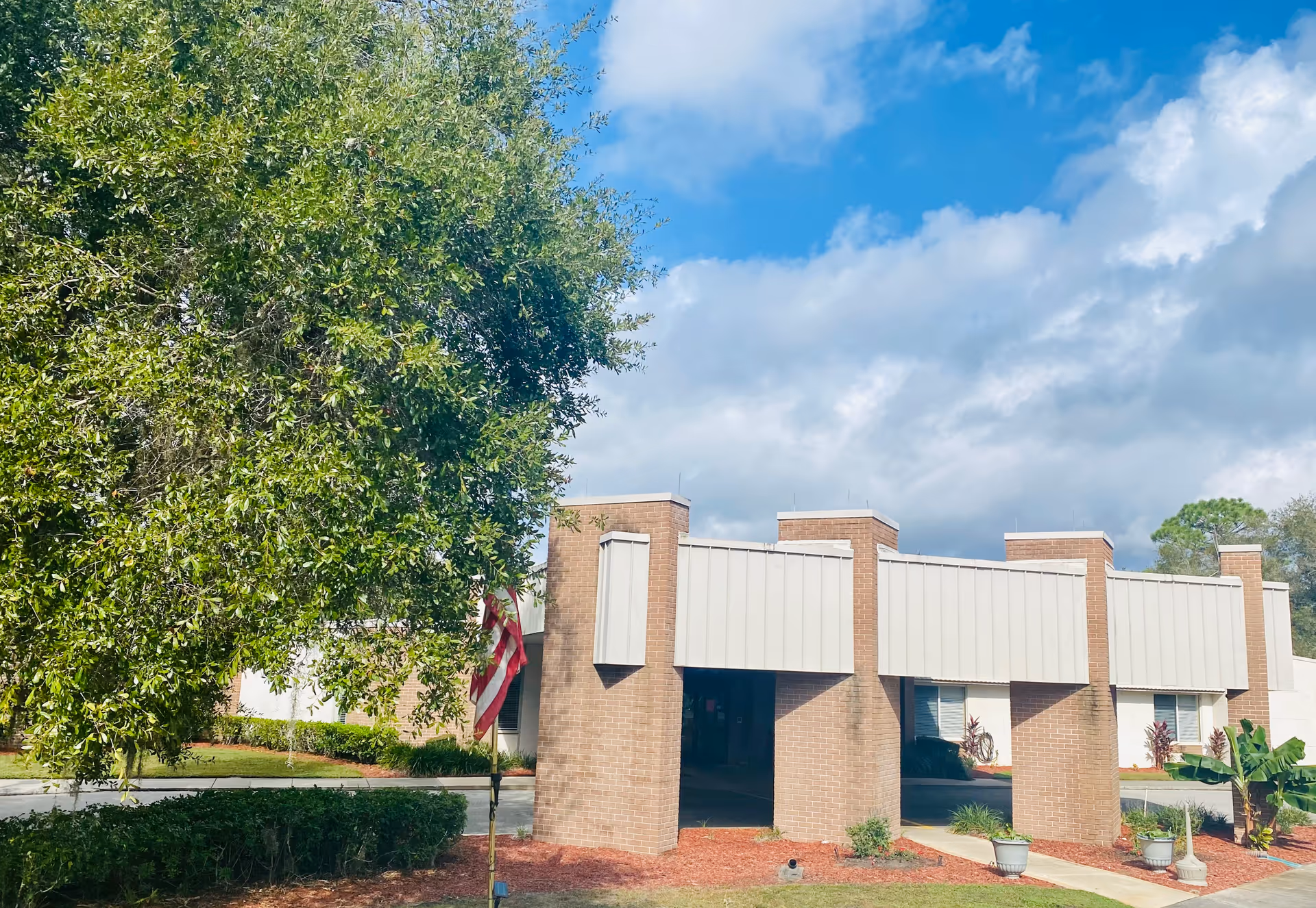 Exterior view of Carrollwood Care Center with brick entrance pillars and a large tree.