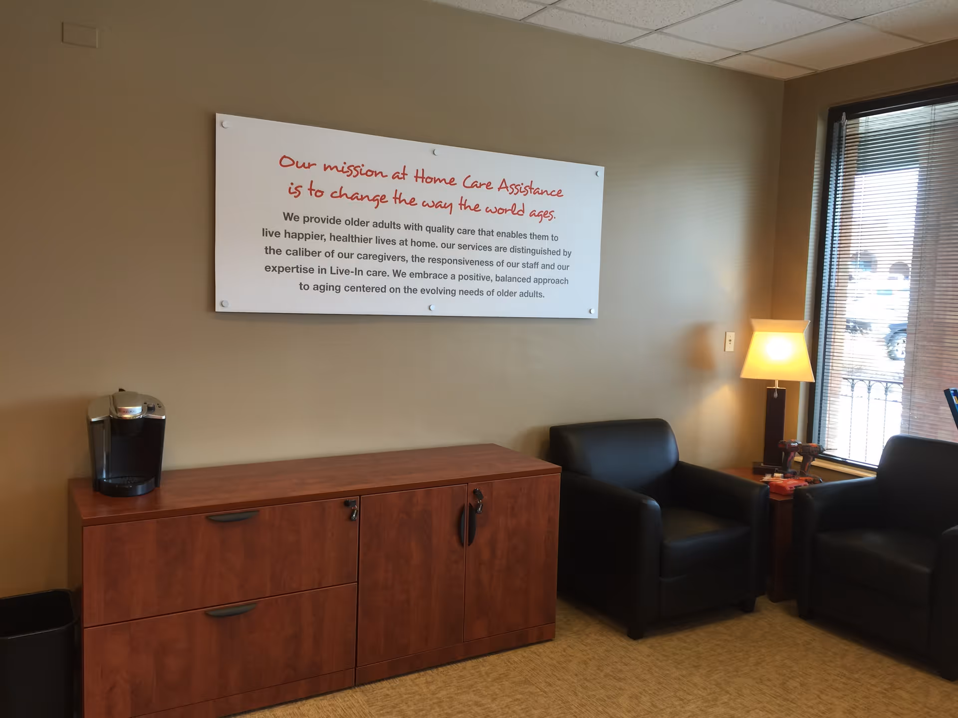 Lounge area with black leather chairs, a wooden cabinet, coffee maker, and wall sign