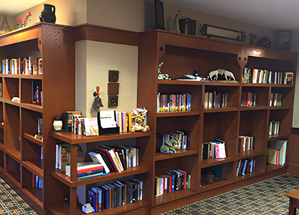 Large wooden bookcase filled with books and decorative items in a carpeted common room.