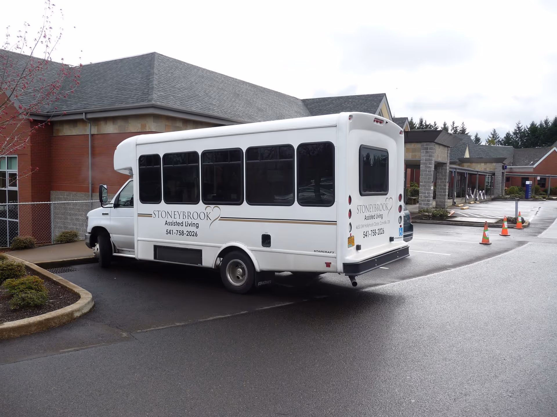 White Stoneybrook shuttle bus parked outside a senior living facility entrance.