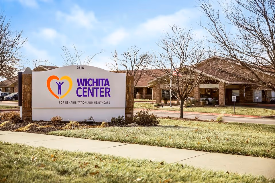 Front sign for Wichita Center for Rehabilitation and Healthcare on a lawn with the facility building behind it.