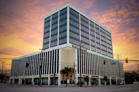 Exterior view of a tall, modern building at a street corner during sunset.