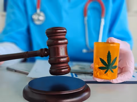 Gavel and cannabis bottle on a desk with a medical professional in scrubs in the background.