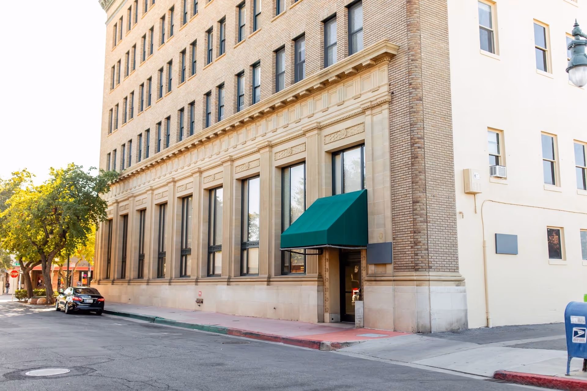 A brick, multi-story building with a green canopy over the entrance on a city street.