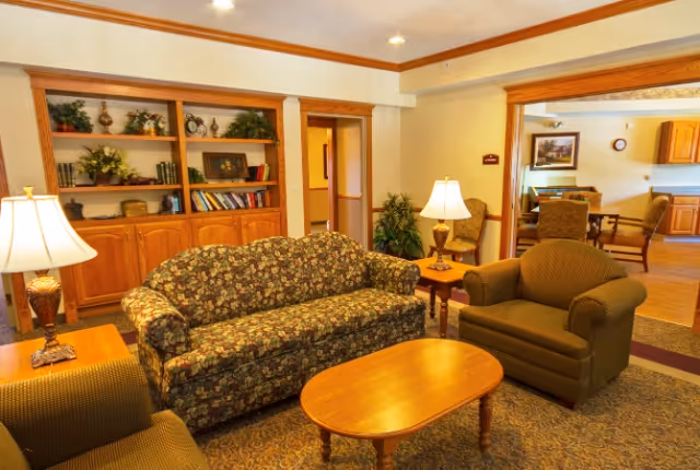 Comfortable living room with a floral sofa, armchairs, a wooden coffee table, lamps, and a built-in bookcase opening to a dining area.
