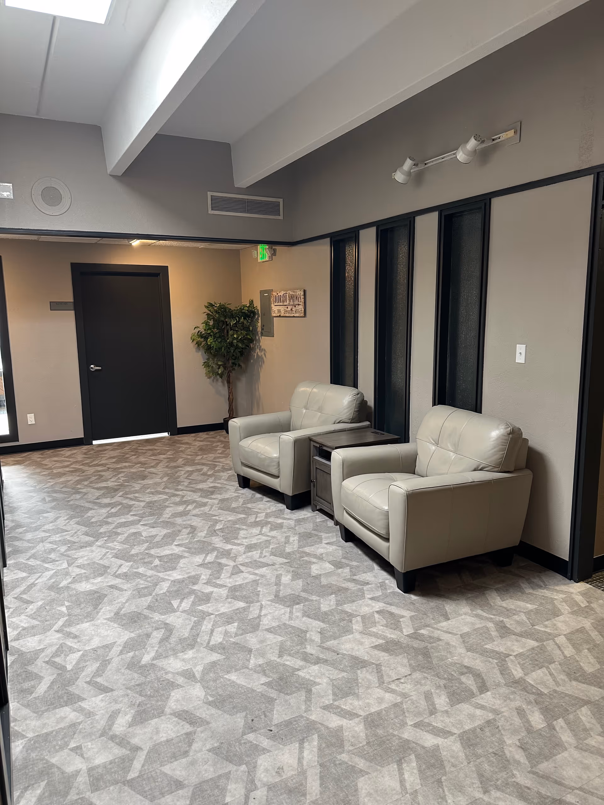 Interior lounge area with two beige leather armchairs, a side table, and a potted plant.