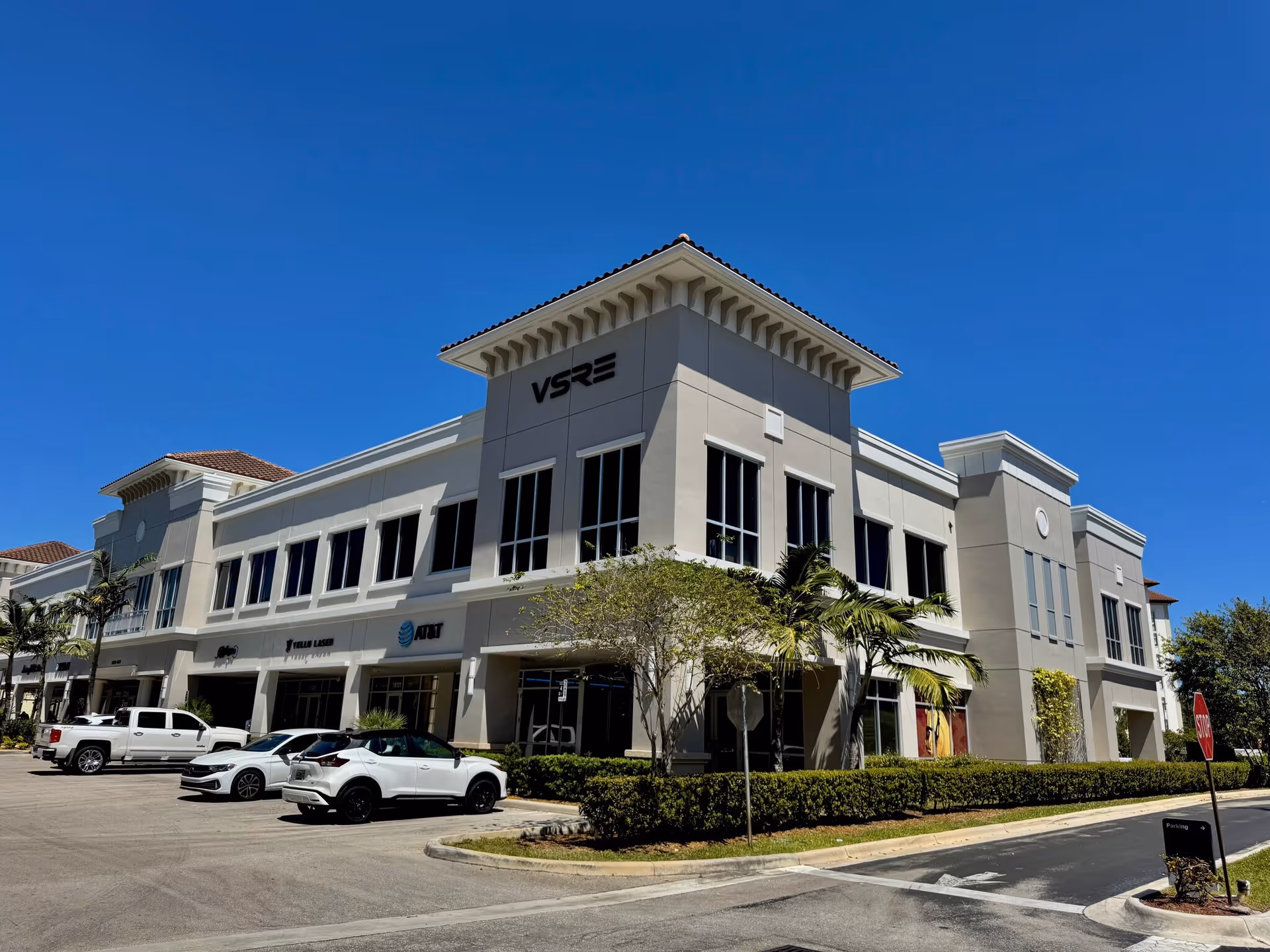 Exterior view of a large light-colored senior living facility with cars in the parking lot.
