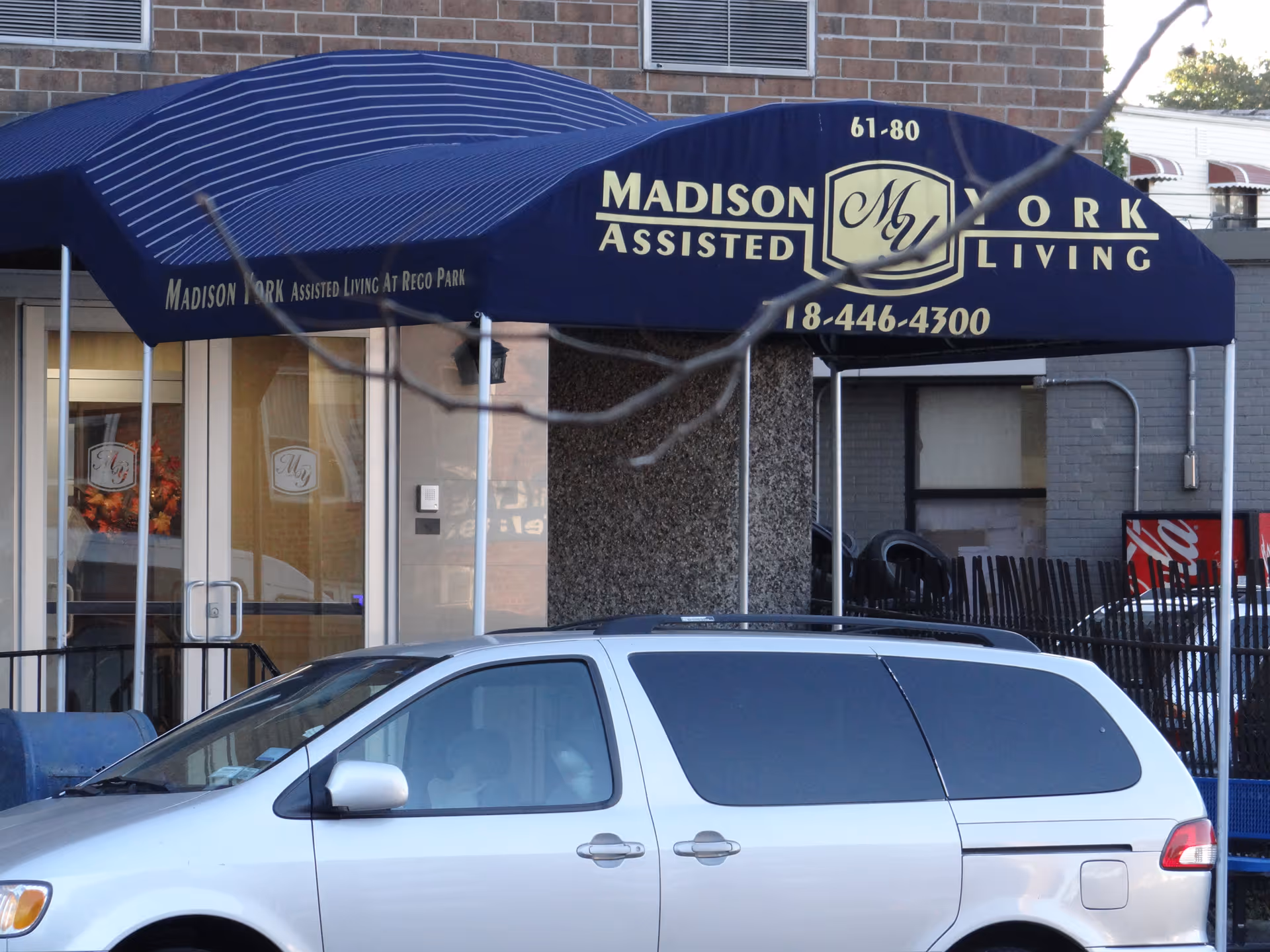 Blue awning with Madison York Assisted Living signage over a building entrance, with a parked van.