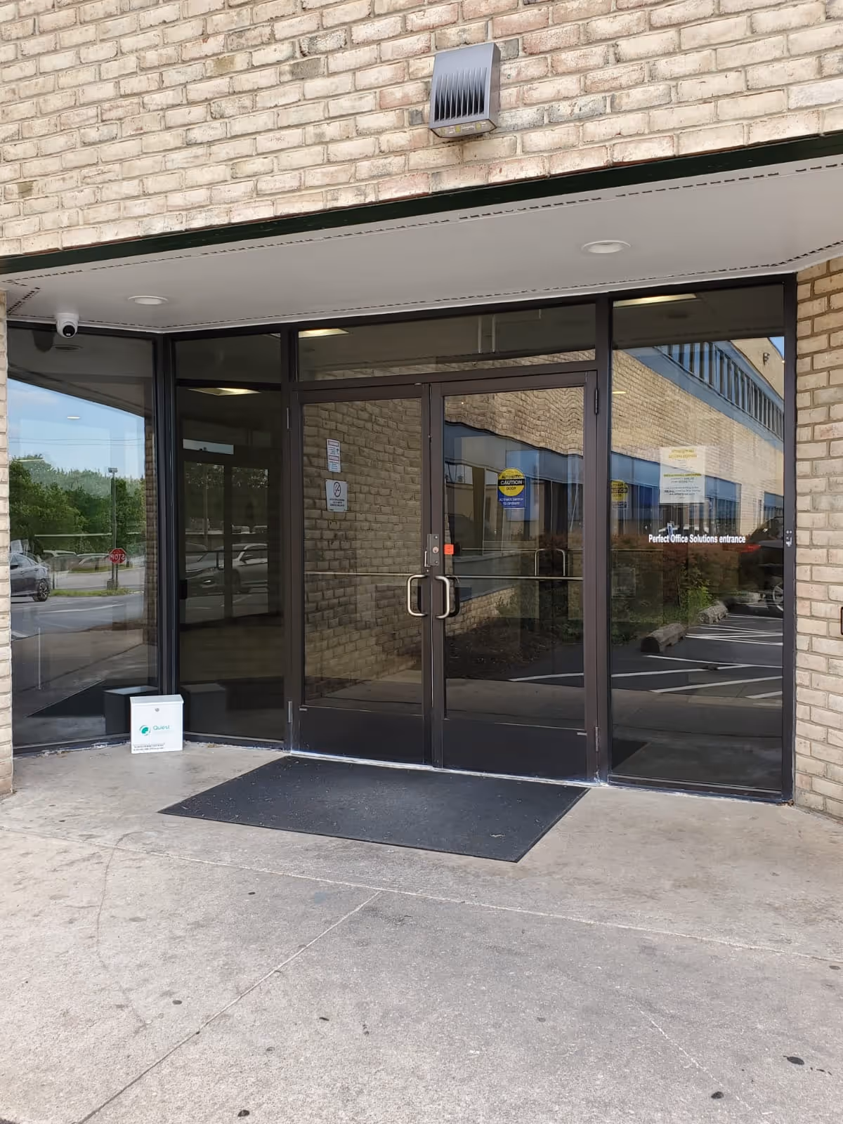 Glass entrance doors of a brick building with a black frame and security camera.