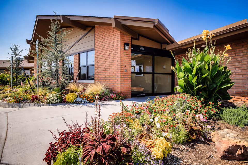 Brick building entrance with glass doors and vibrant landscaping along a walkway.