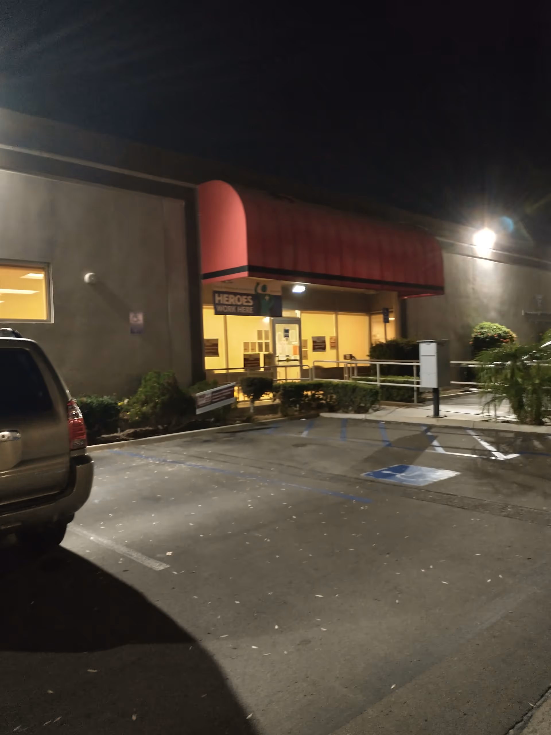 Nighttime exterior of a building with a red awning and parking lot