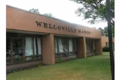 Exterior view of a brick building labeled Wellsville Manor with a grassy lawn.