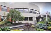 Exterior view of a curved, modern senior care building with a landscaped entrance.