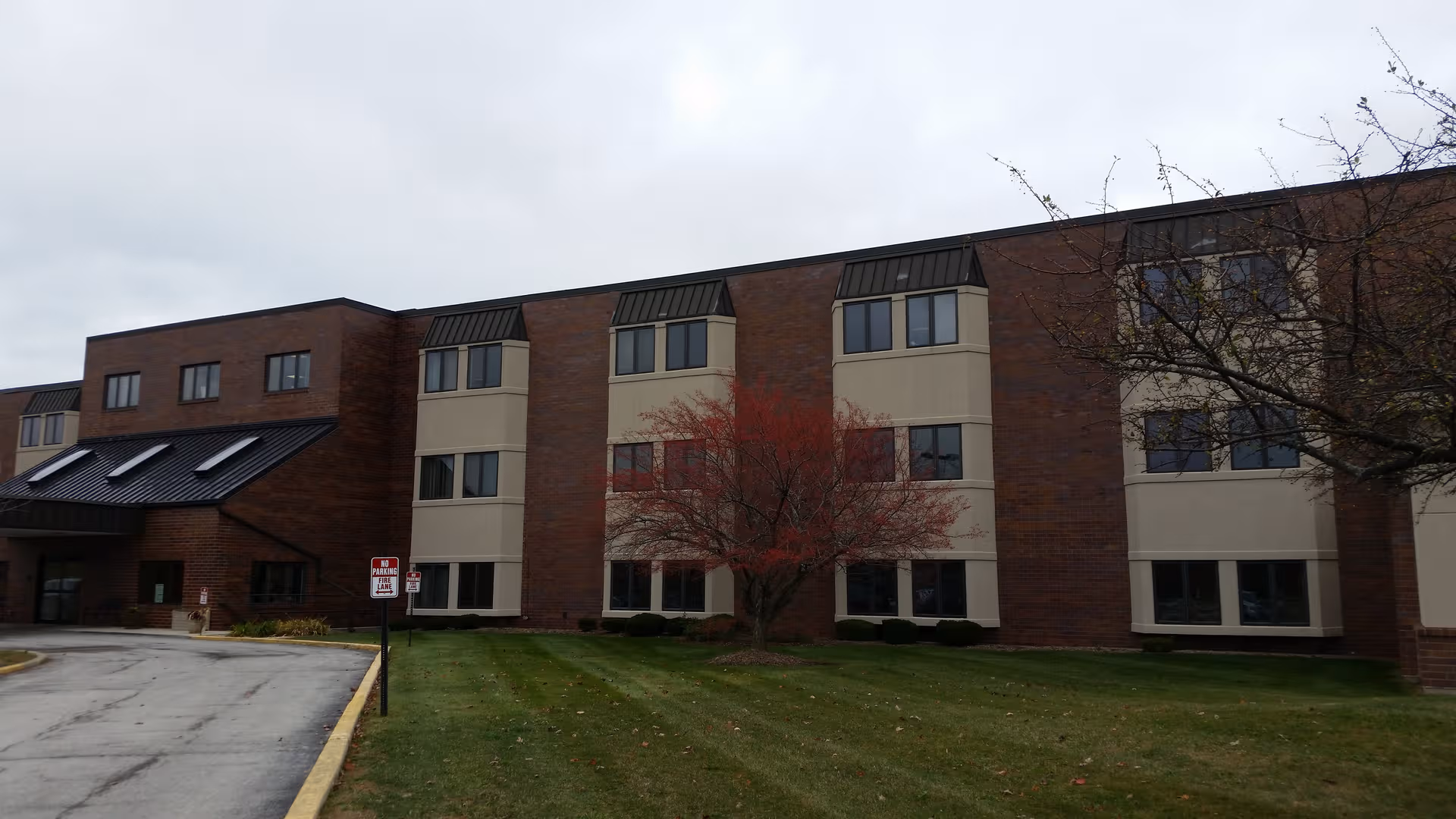 Brick senior living facility exterior with numerous windows and a green lawn.