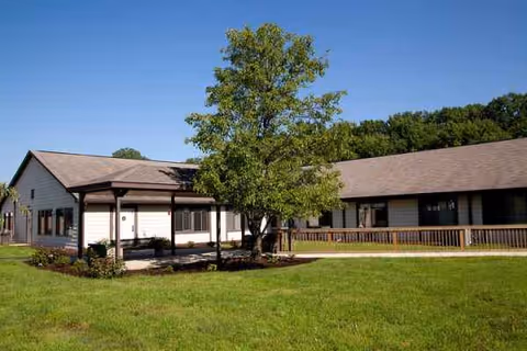 Single-story nursing facility with a covered entrance, a central tree, and a grassy lawn under a clear blue sky.