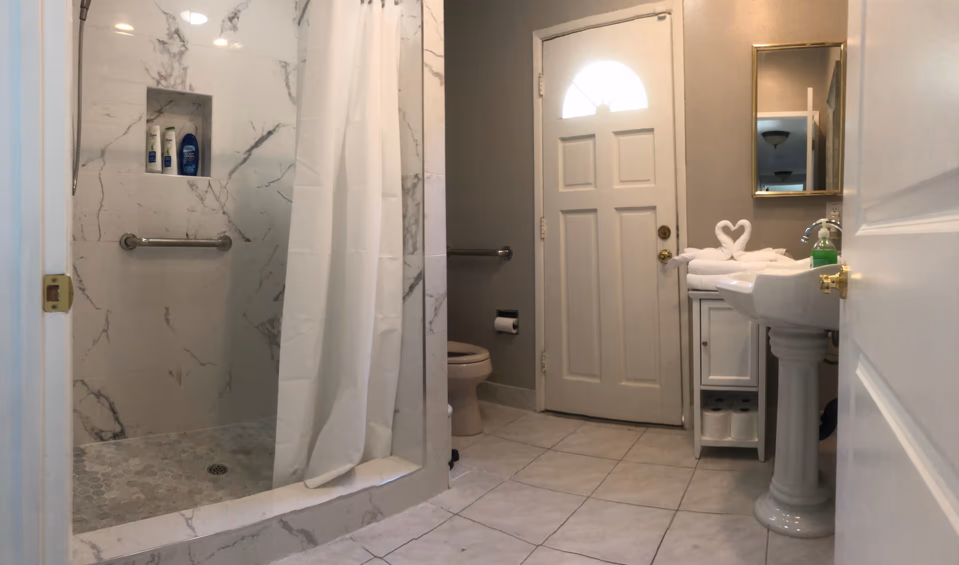 Marble-tiled bathroom with walk-in shower, sink, mirror, and toilet in a senior living facility.