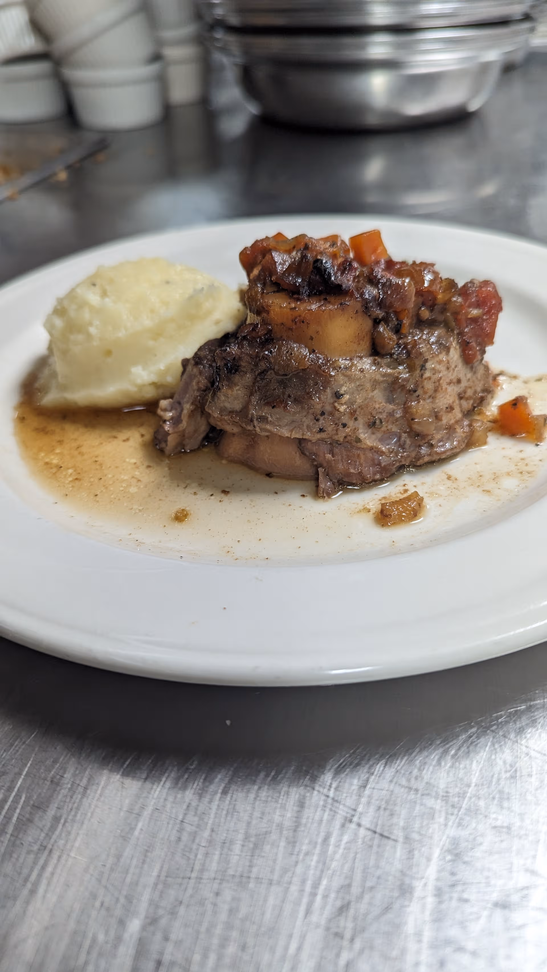 Plate of beef with vegetables and mashed potatoes on a stainless steel kitchen counter.