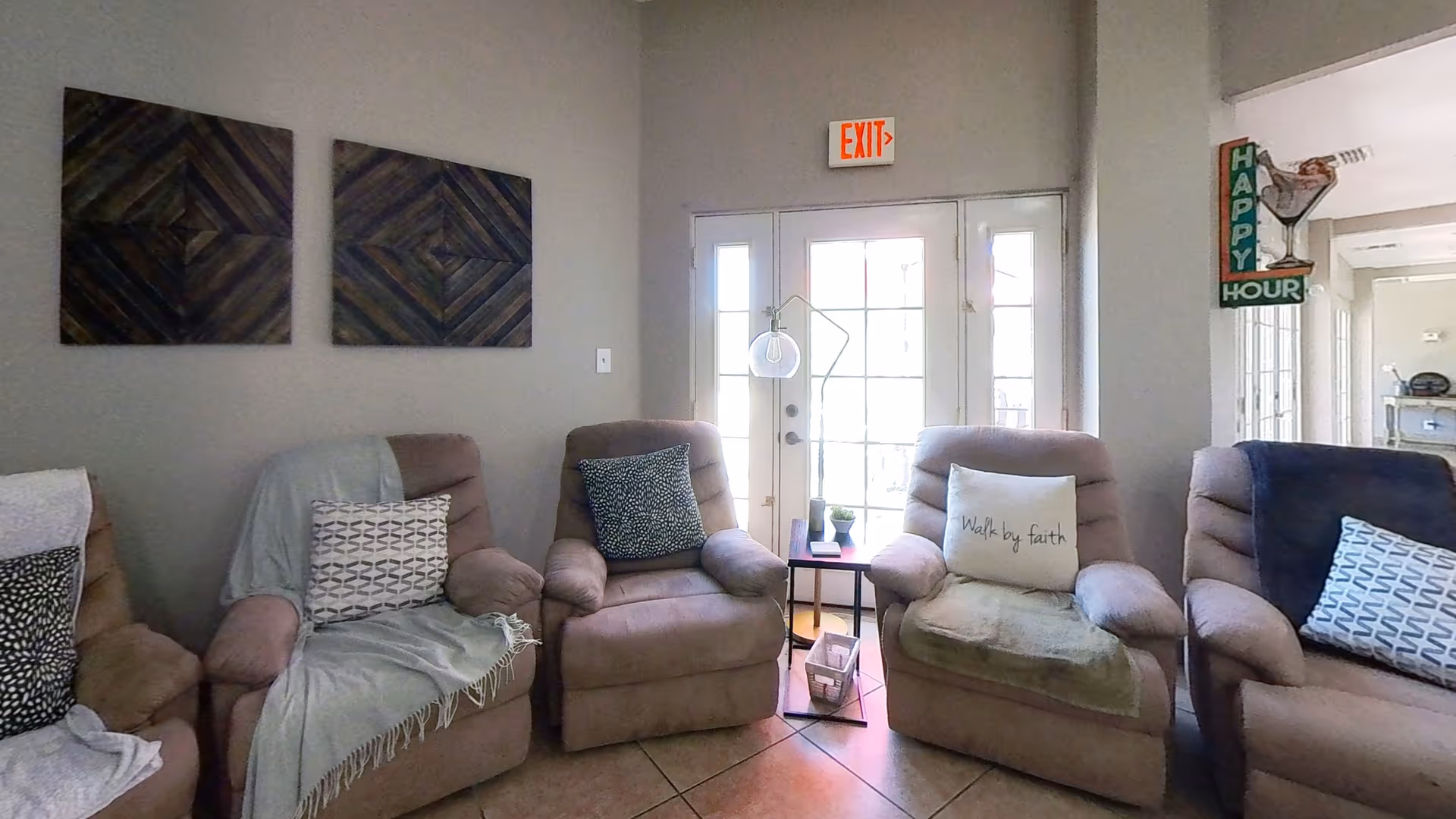 Row of beige recliners with cushions around a small table near exit doors.
