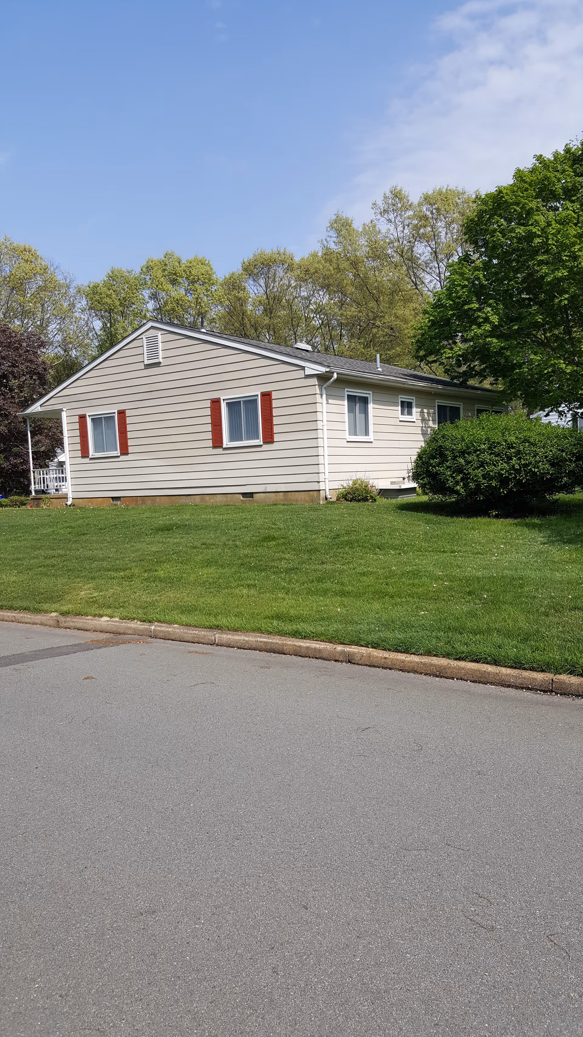 Single-story beige building with red shutters, green lawn, and trees in a suburban setting.