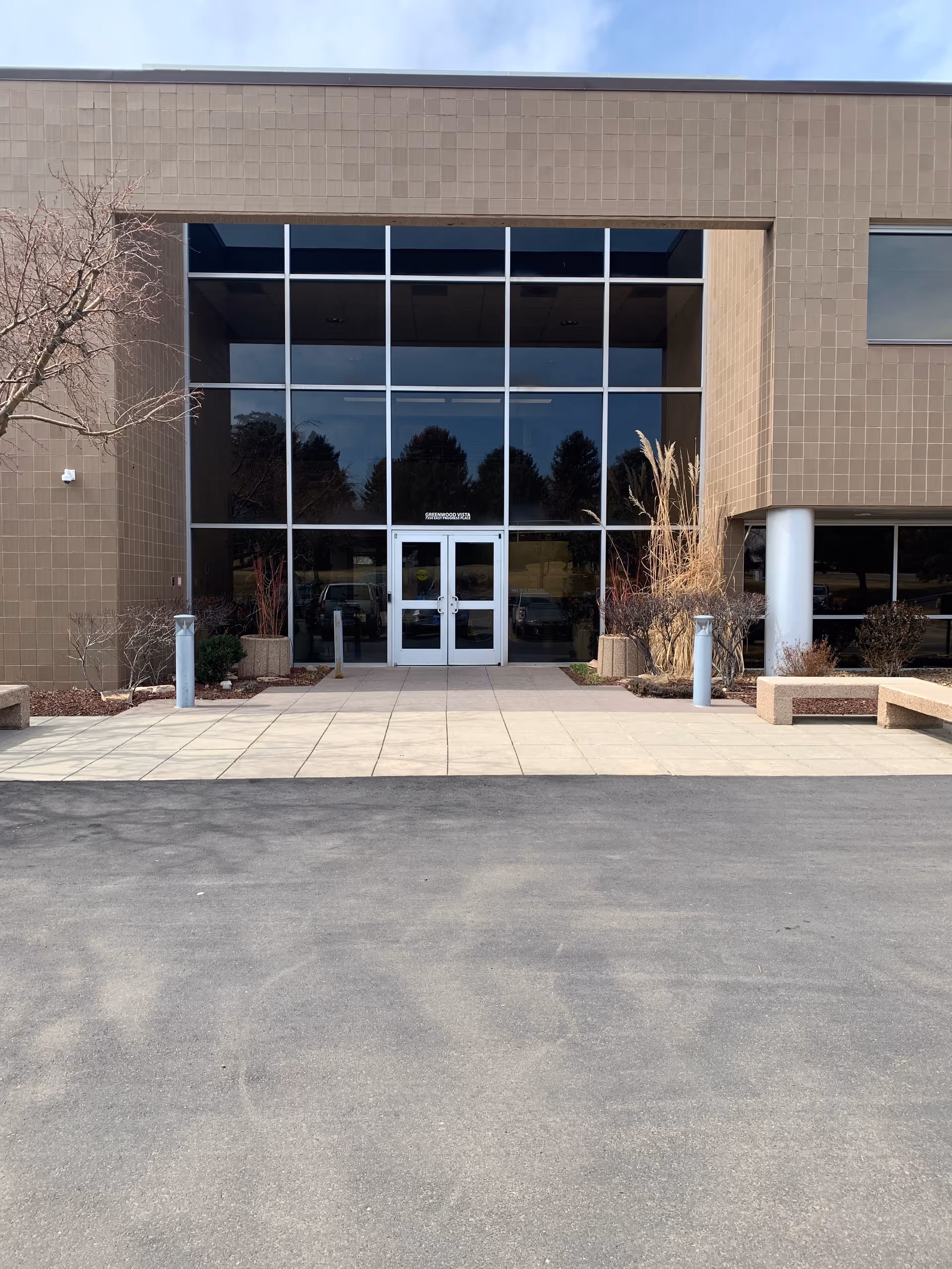 Front entrance of a modern building with large glass doors and tidy landscaping.