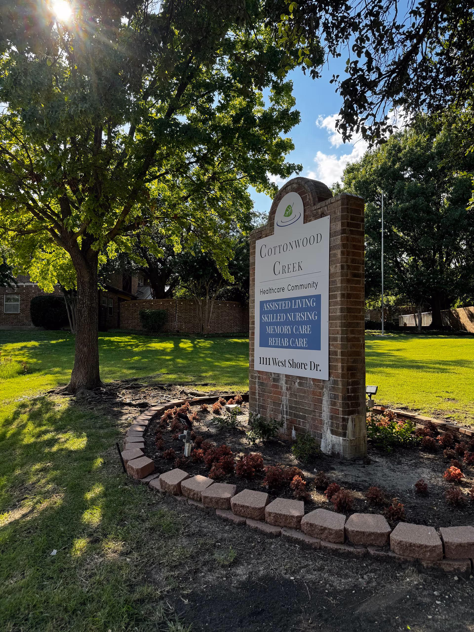 A brick sign for Cottonwood Creek Healthcare Community sits on a manicured lawn.