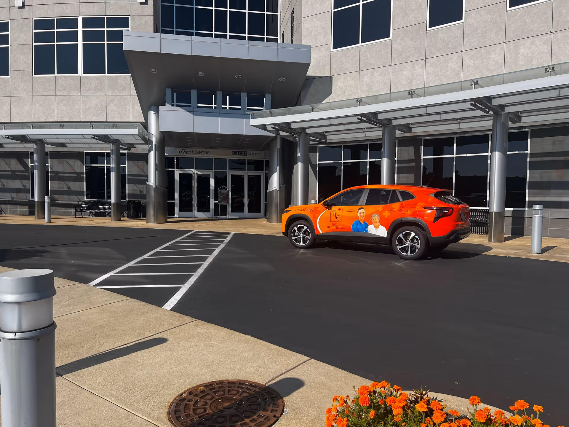 Exterior view of a TLC Home Healthcare building with an orange promotional vehicle parked outside.