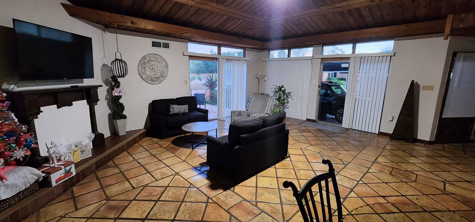 Spacious living room with tiled floor, black sofas, TV, fireplace, and sliding doors.