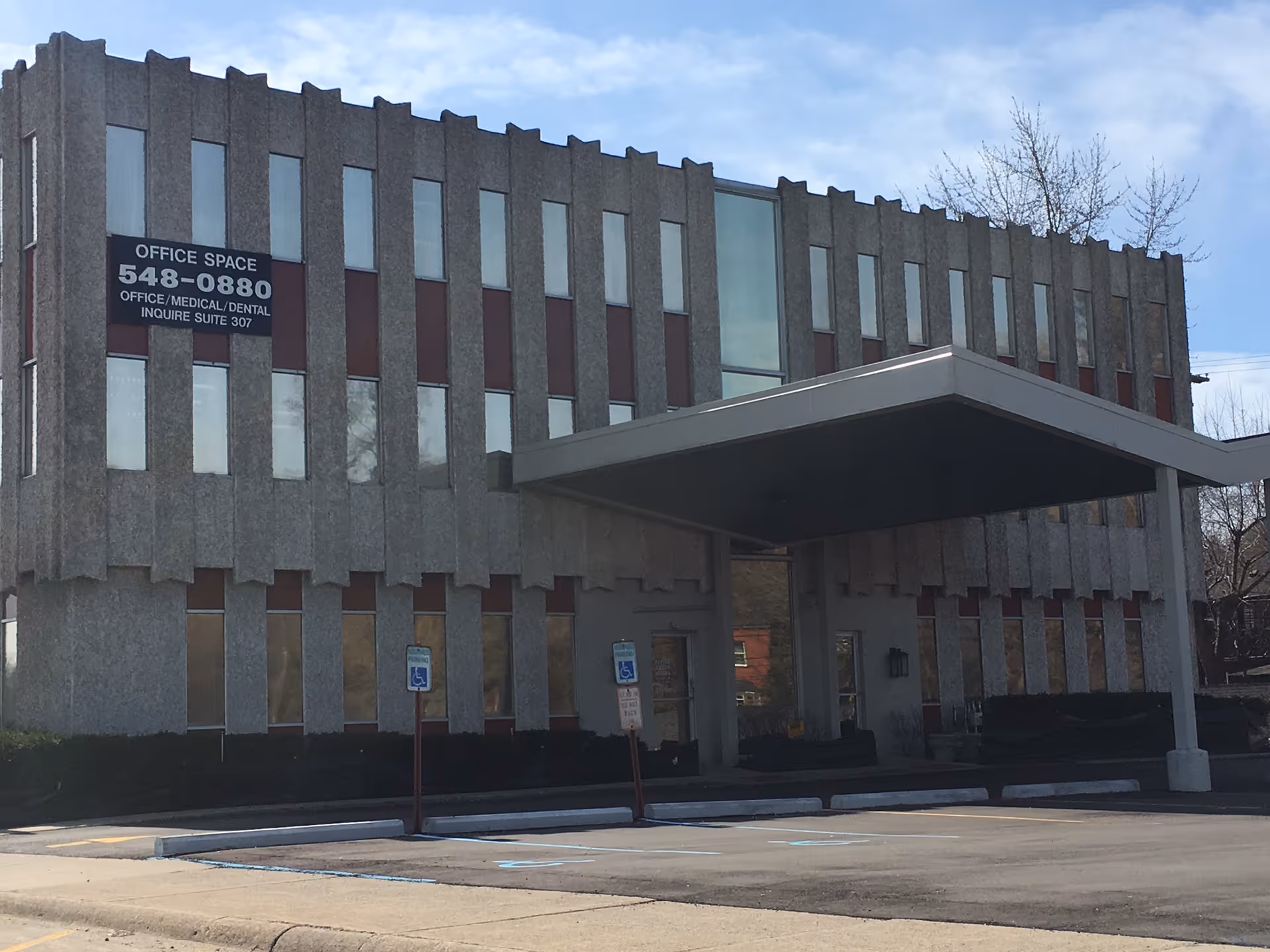 Gray concrete office building with a large canopy entrance and a sign.