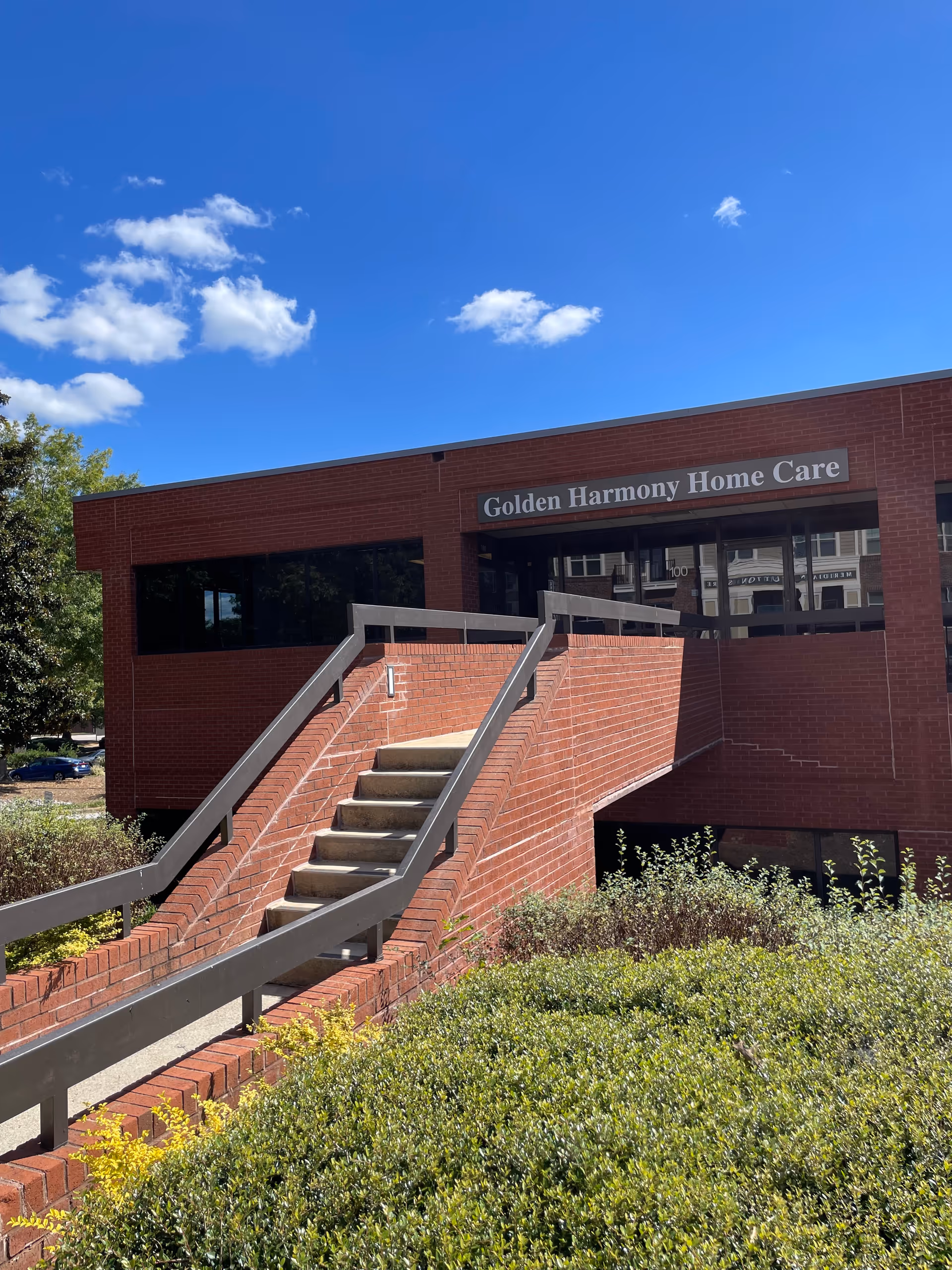 Brick senior care building with a long staircase leading to glass entrance under blue sky.