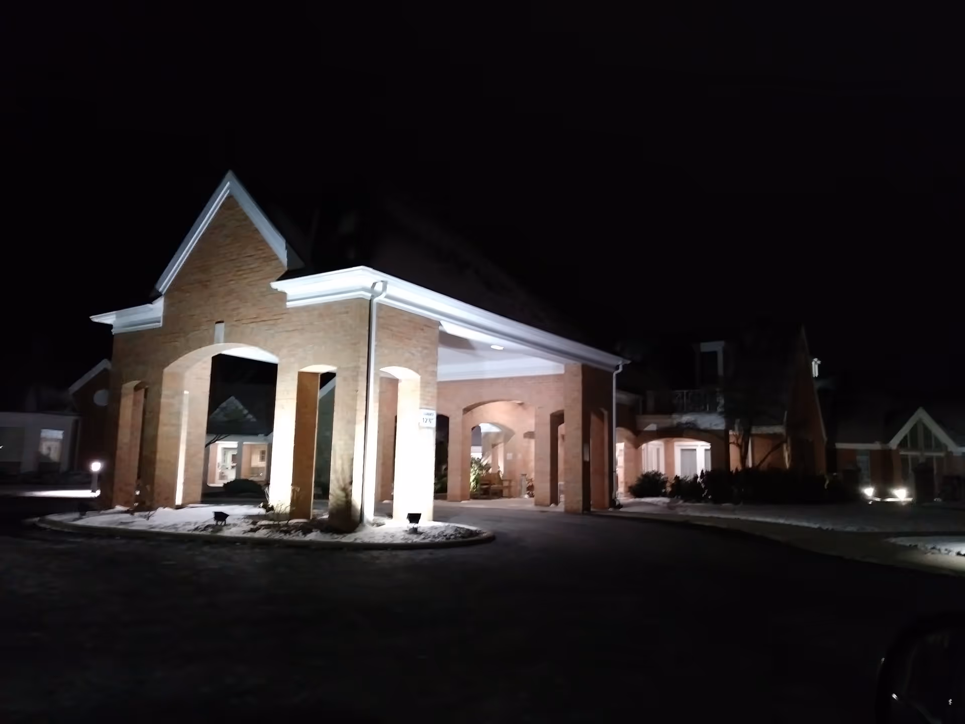 Night view of The Parkvue Community entrance with brick arches and illuminated driveway.