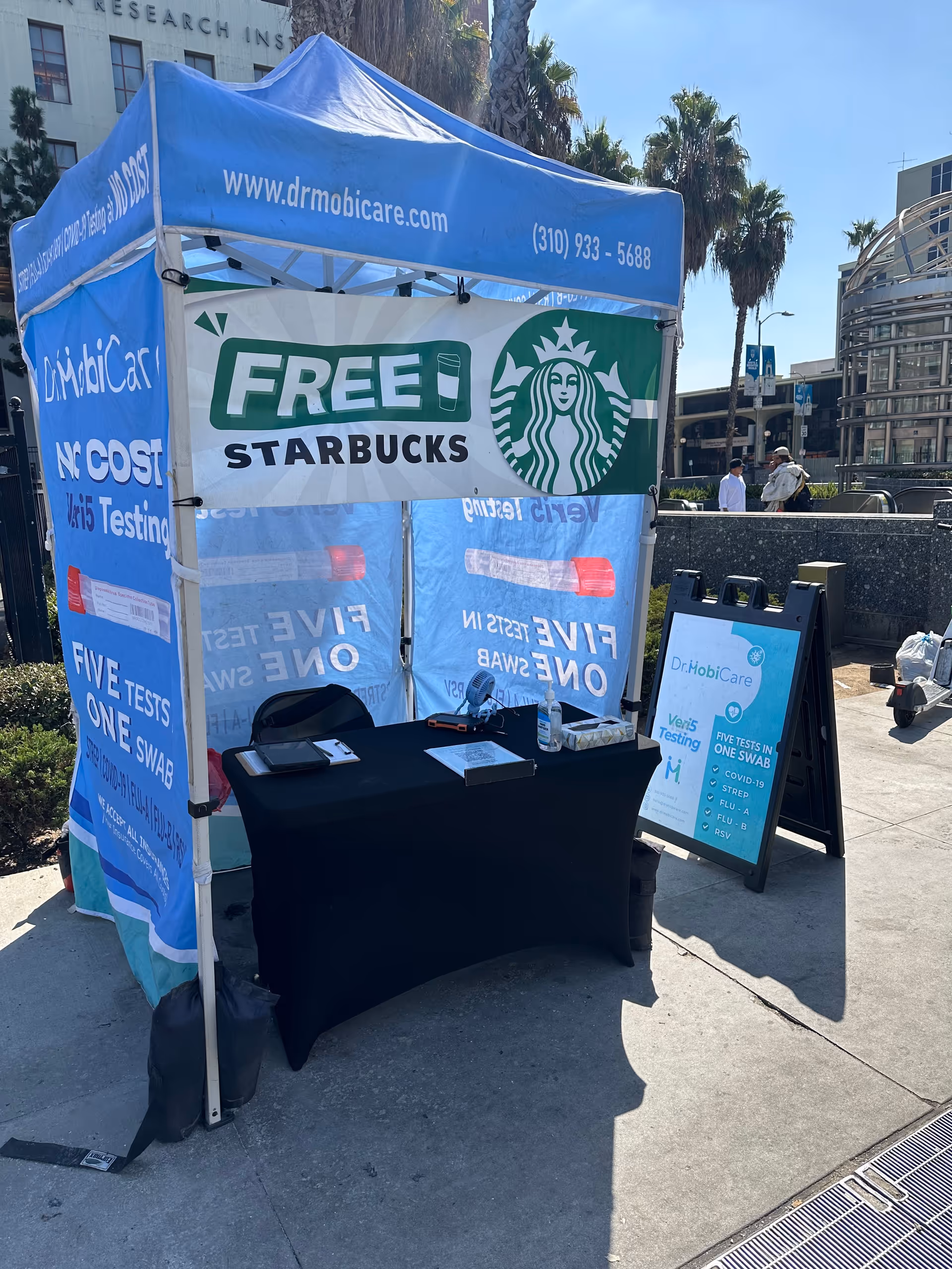 Blue outdoor promotional tent advertises Free Starbucks with a table and banners.