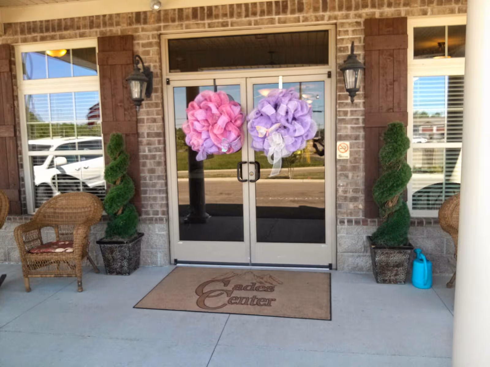 Double glass doors with pink and purple wreaths, flanked by spiral topiary, on a brick entry.