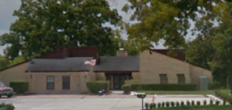 Front view of Rose Hill Senior Living building with parking lot, flag, and trees.
