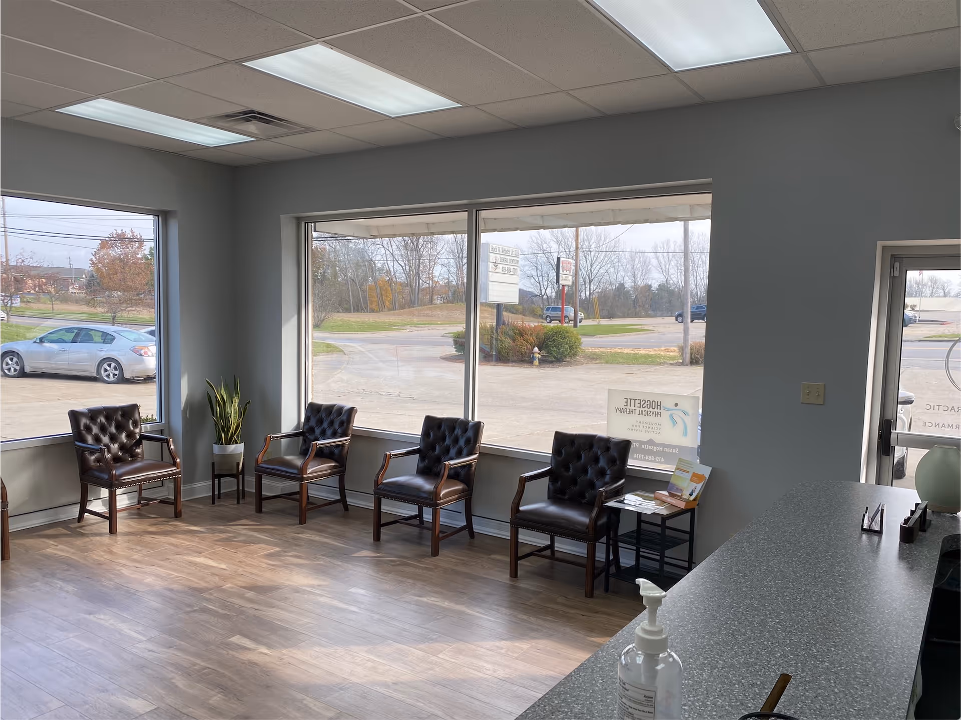 Modern waiting area with four leather chairs along windows and a reception counter.