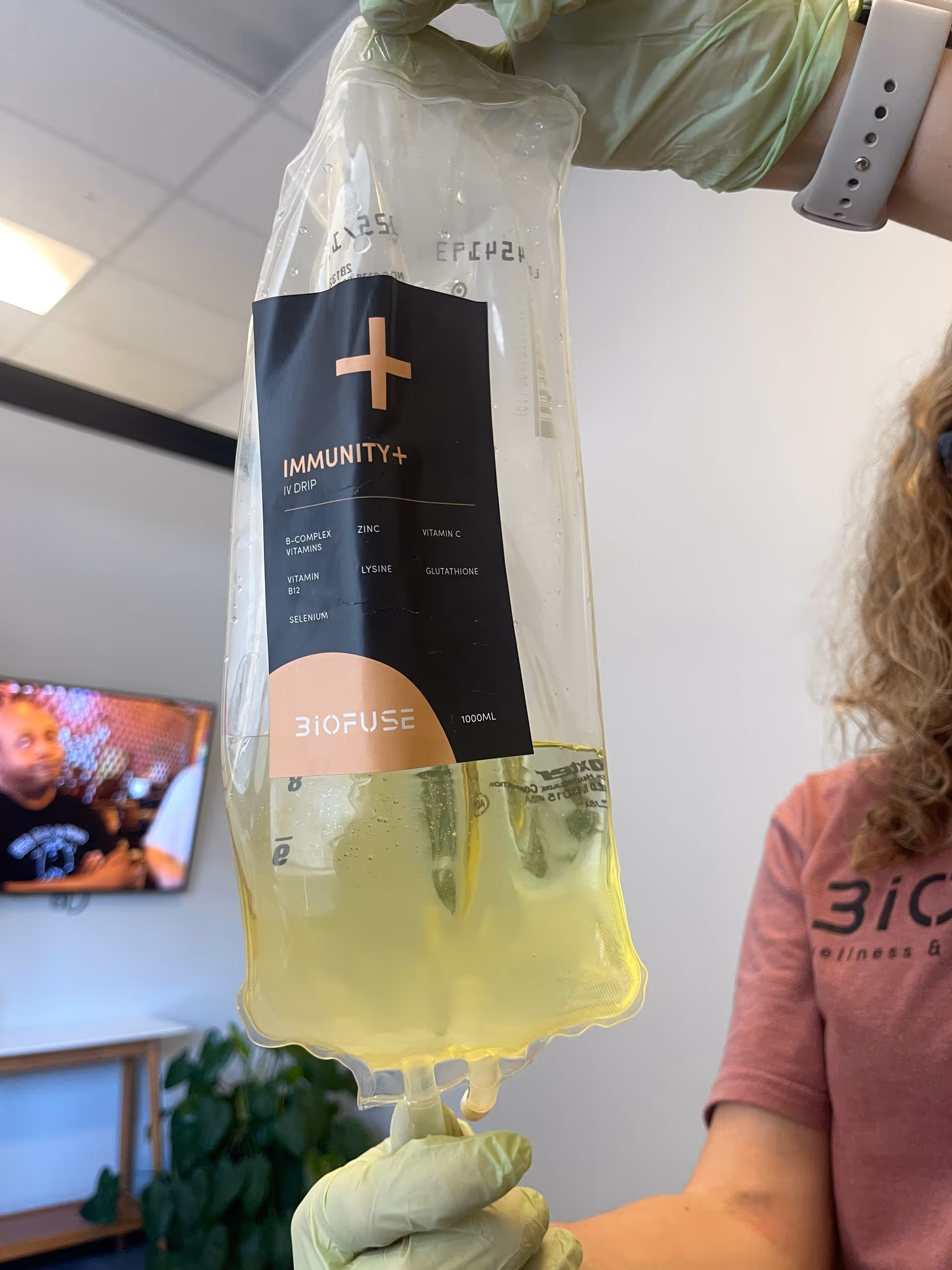 IV drip labeled Immunity+ held by gloved hands in a medical facility.