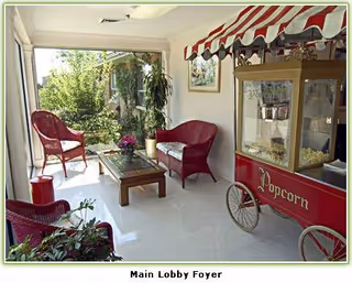 A bright lobby area with red chairs, a popcorn cart, and potted plants.