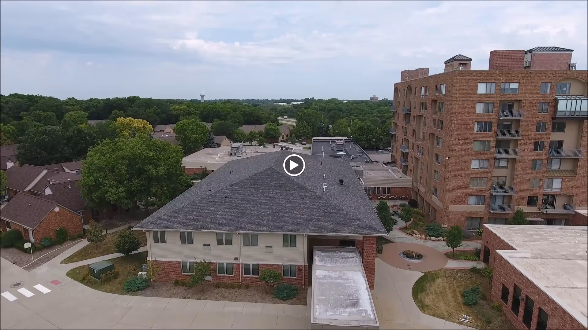 Aerial view of a senior living facility named The Lindens at Green Hills, showing multiple connected buildings with brick and light-colored exteriors, surrounded by trees and greenery under a partly cloudy sky.