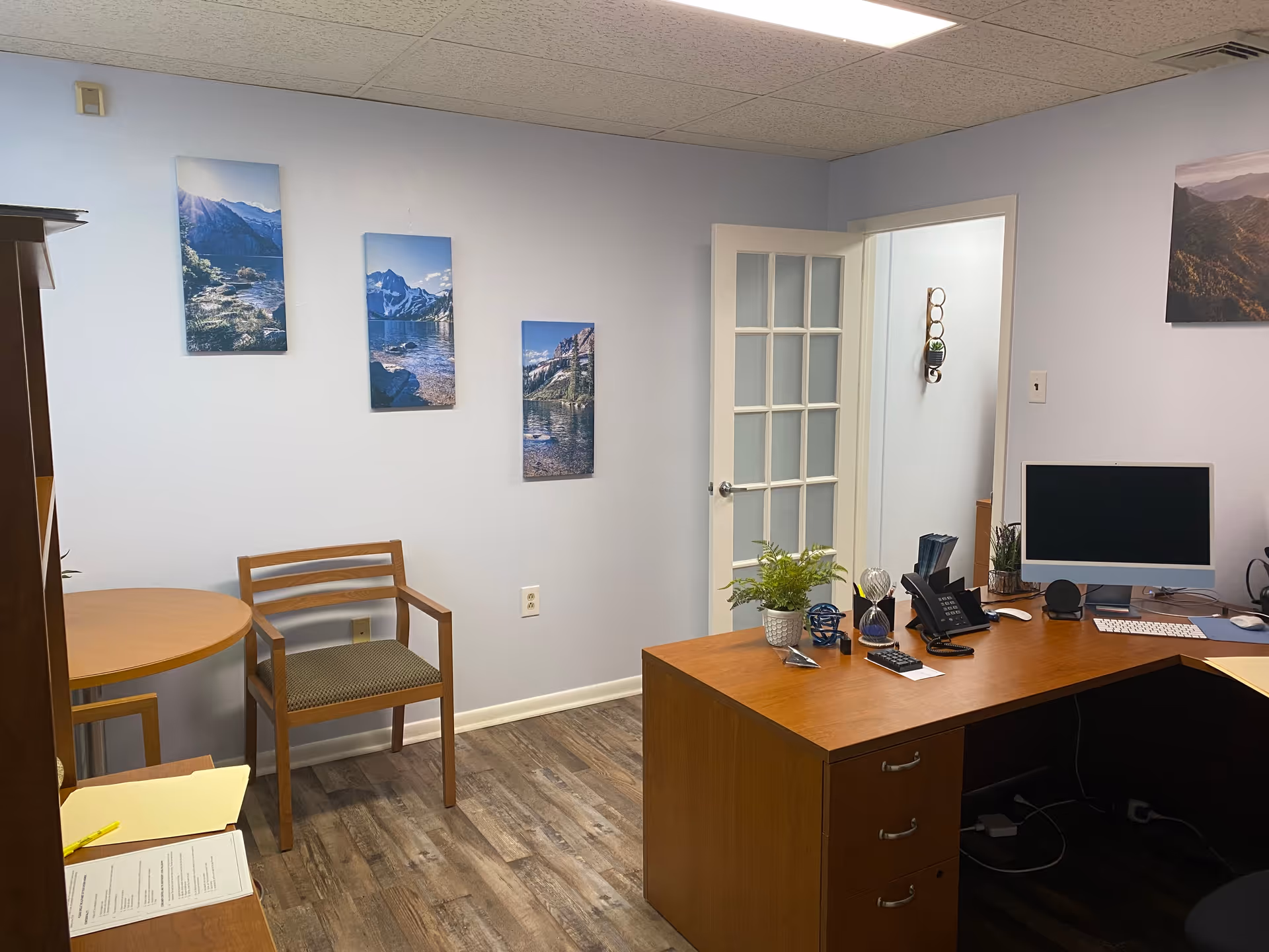 Office desk with computer, phone, plants, and mountain wall art in a reception area.