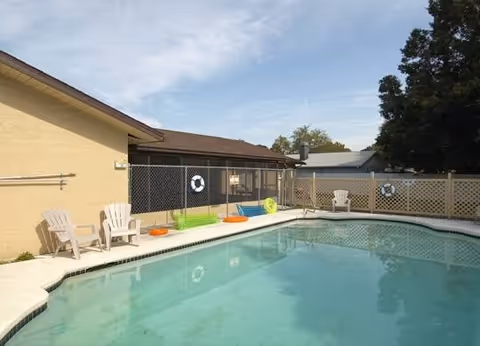 Outdoor pool area with lounge chairs, life rings, and a fenced perimeter.