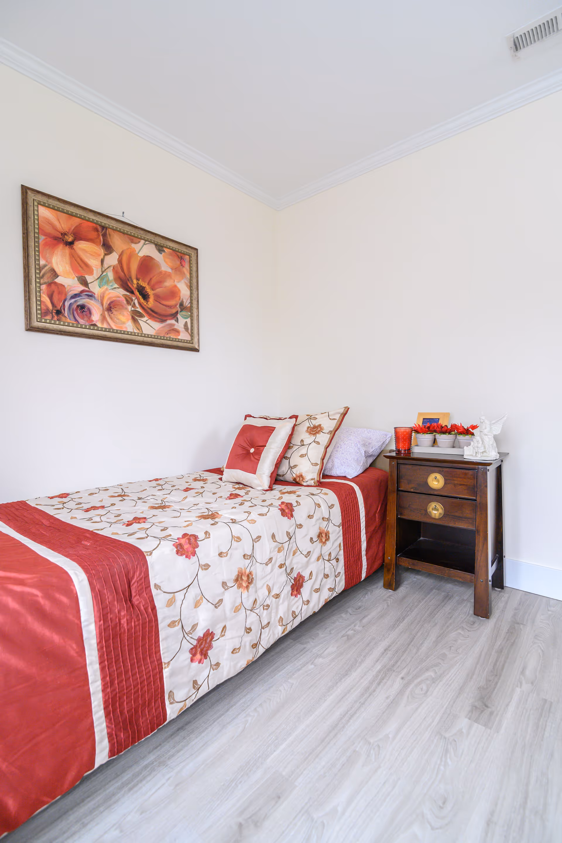 A neatly made bedroom with floral bedding, decorative pillows, and a wooden nightstand.